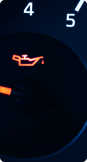 Oil change services in Newport, NH with Promex Auto. Close-up image of a car dashboard oil pressure warning light. The light is illuminated in red, depicting an oil can with a droplet, indicating that the vehicle's oil pressure is low. The background shows a partial view of the gauge with the numbers 4 and 5.