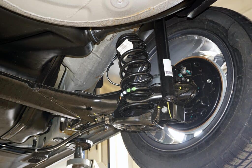 Clunking Noises Driving You Crazy? Suspension Repair Experts at Promex Auto Are Here to Help. Close-up of a car’s suspension system, showcasing the coil spring, shock absorber, and wheel components from underneath the vehicle.