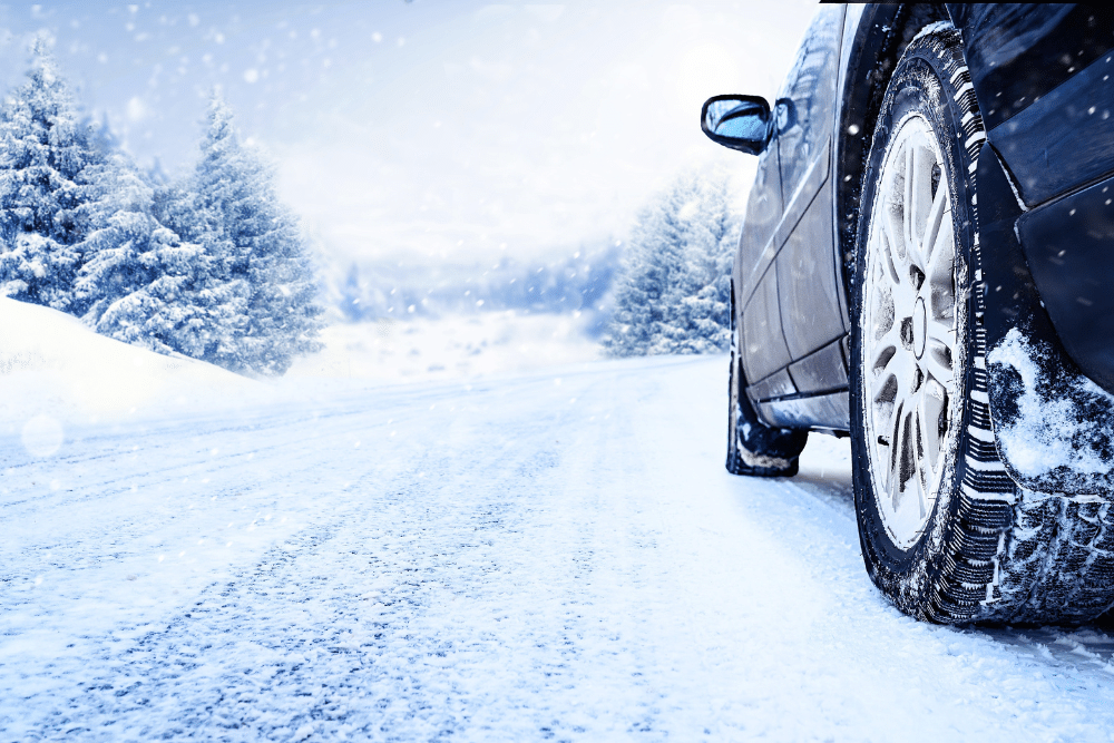 winter car maintenance in Newport, auto repair in Newport, NH at Promex Auto. Close-up of a car tire driving on a snow-covered road, showcasing winter tires and snowy weather conditions.