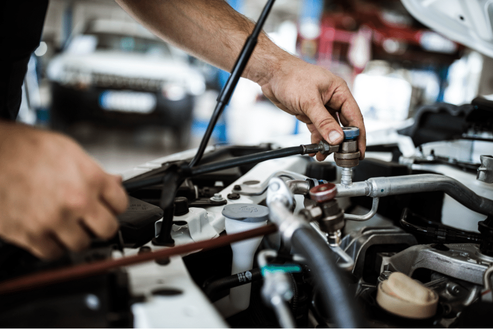 car A/C parts, auto repair in Newport, NH at Promex Auto. Technician connecting a refrigerant hose to a vehicle’s air conditioning system during an A/C recharge service.