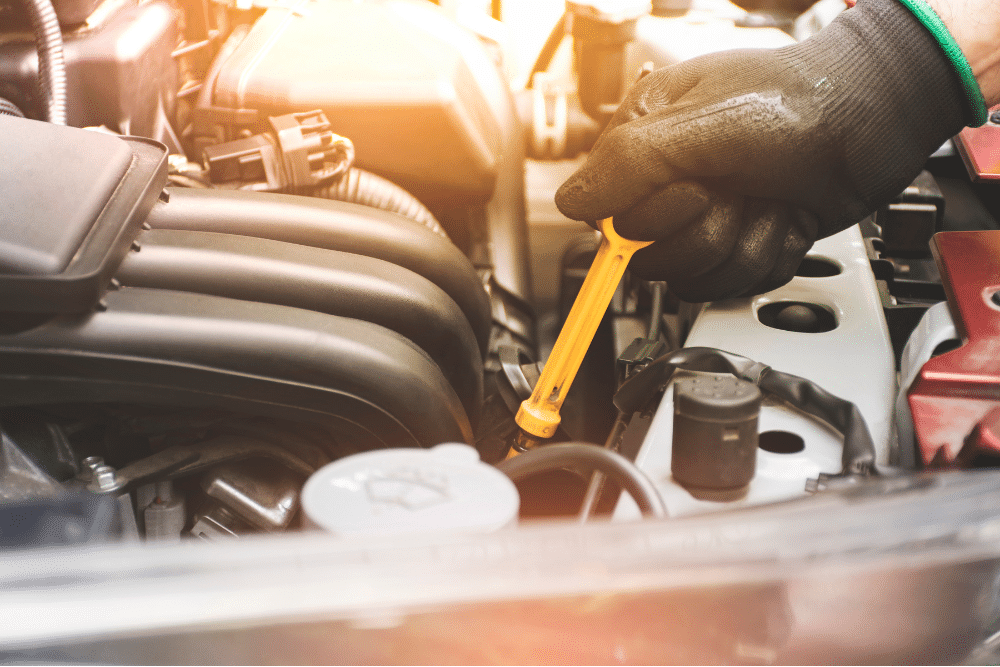 summer car maintenance tips, auto repair in Newport, NH at Promex Auto. Oil level inspection in progress at Promex Auto in Newport, NH. Gloved technician pulling out the dipstick to check fluid during routine maintenance.