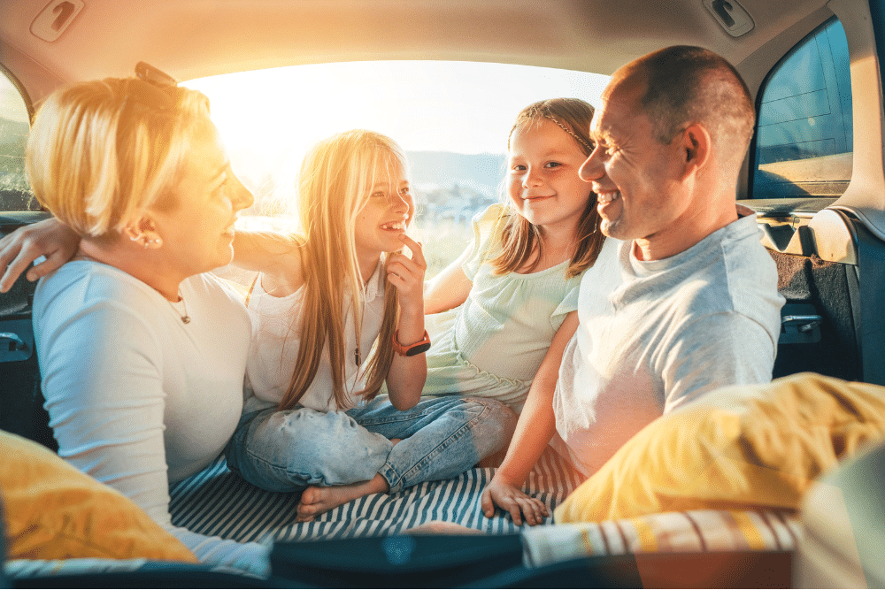 Vehicle Inspection in Newport, NH by Promex Auto. Family sitting together in the back of a vehicle at sunset, smiling and talking, highlighting a warm and relaxed family travel moment.